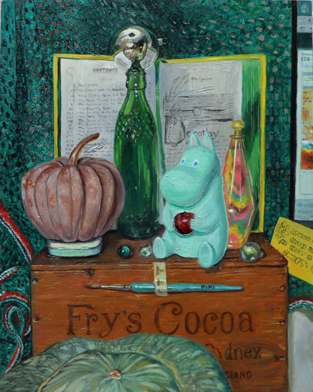 Oil painting featuring a futsu pumpkin, green bottle, mirrored bauble, moomin toy holding an Apple, a coloured sand bottle, and marbles, all on top of a wooden Fry’s Cocoa box and behind these items is an open yellow book (The Wizard of Oz) with green page edges. There is a green crocheted blanket with red, white and black trim as the back drop. In front of the Cocoa box is a green striped pumpkin.