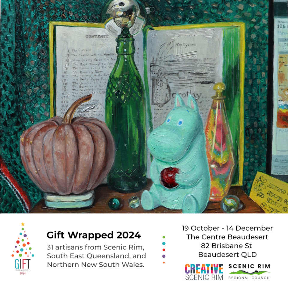 Flyer for gift wrapped exhibition. Info reads:  
				19 October - 14 December 2024
			    The Centre Beaudesert
			    82 Brisbane St, Beaudesert QLD.
			    Thirty-one artisans from Scenic Rim, South East Queensland and Northern New South Wales. 
			   
			    The painting featured is a still life featuring a futsu pumpkin, green bottle, mirrored bauble, moomin toy holding an Apple, a coloured sand bottle, and marbles, all on top of a wooden Fry’s Cocoa box and behind these items is an open yellow book (The Wizard of Oz) with green page edges. There is a green crocheted blanket with red, white and black trim as the back drop.